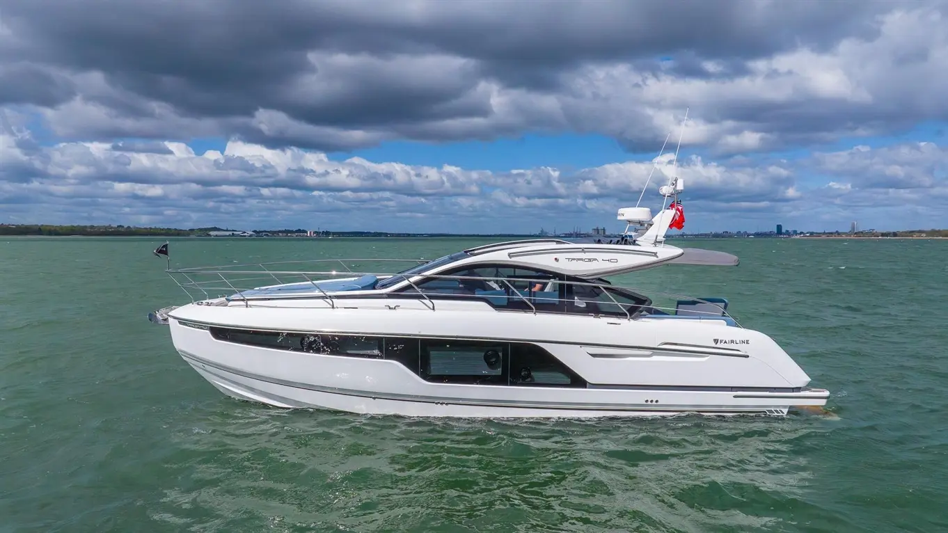 A Fairline Targa 40 motor yacht gliding through green waters under a cloudy sky, showcasing luxury and elegance on the sea.